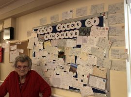 Edna pictured next to the post cards of kindness wall at Alderwood Care Home.Image Credit: Abigail Walker
